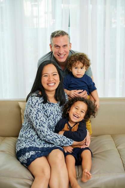 Feliz alegre familia multiétnica de cuatro personas sentadas en el sofá en casa y mirando a la cámara