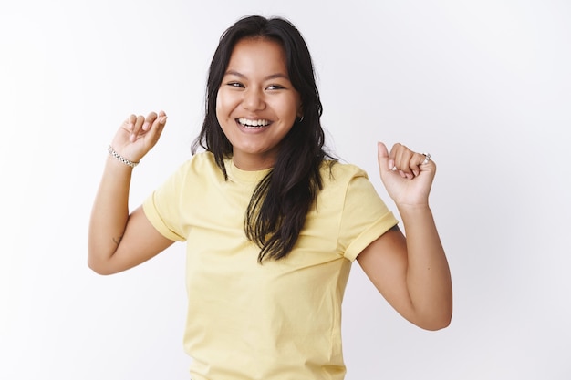 Feliz y alegre joven despreocupada haciendo danza de la victoria como celebrando el final del proyecto levantando las manos moviendo el ritmo de la música mirando a un lado y sonriendo ampliamente, disfrutando de tener un día increíble