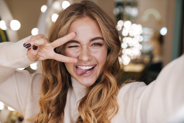 feliz alegre joven hermosa tomar un selfie en salón mostrando gesto de paz.