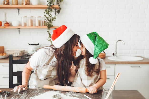 Feliz y alegre madre e hijo con sombreros de Papá Noel están cocinando galletas navideñas en la cocina año nuevo y Navidad