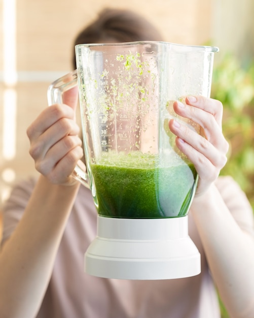 Feliz y alegre mujer caucásica en una camiseta en su cocina hace un batido verde