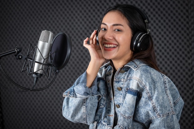 Feliz alegre muy sonriente del retrato de la joven vocalista asiática con auriculares grabando una canción frente al micrófono en un estudio profesional