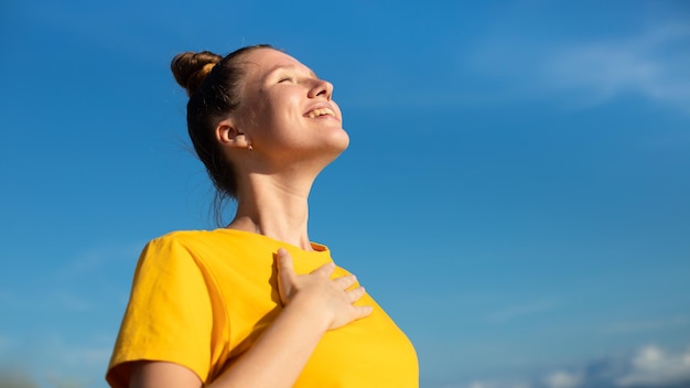 Feliz, alegre, positiva, joven, hermosa, sintiéndose, mujer despreocupada, está disfrutando de las vacaciones en el día soleado de verano, tomando el sol, bronceándose y sonriendo, concepto de libertad de felicidad en el fondo natural del cielo