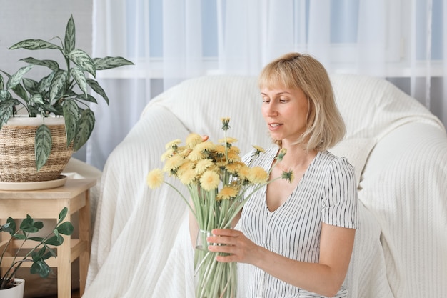 Feliz, alegre, sonriente mujer madura de mediana edad en la sala de estar, con un ramo de flores amarillas.