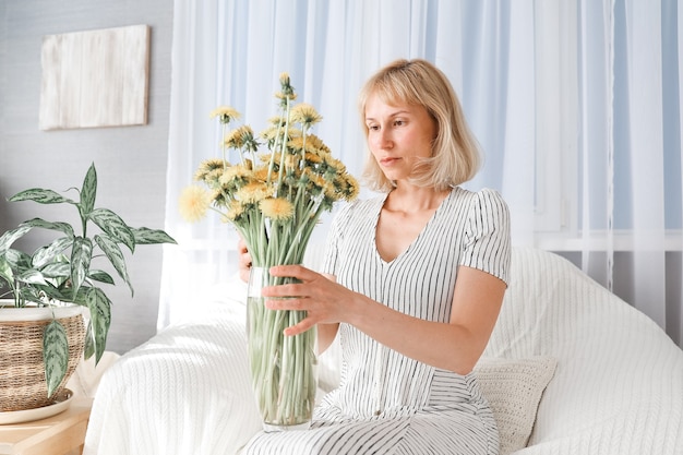 Feliz, alegre, sonriente mujer madura de mediana edad en la sala de estar, con un ramo de flores amarillas.