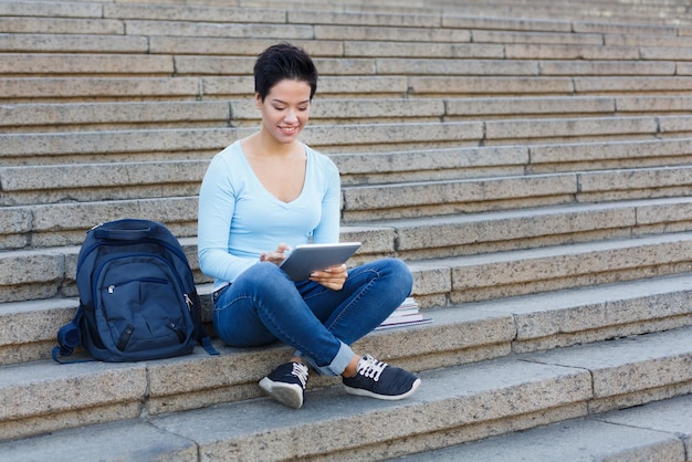Feliz aluna de cabelos curtos com tablet e mochila sentada na escada. Conceito de tecnologia, educação e trabalho remoto, espaço de cópia