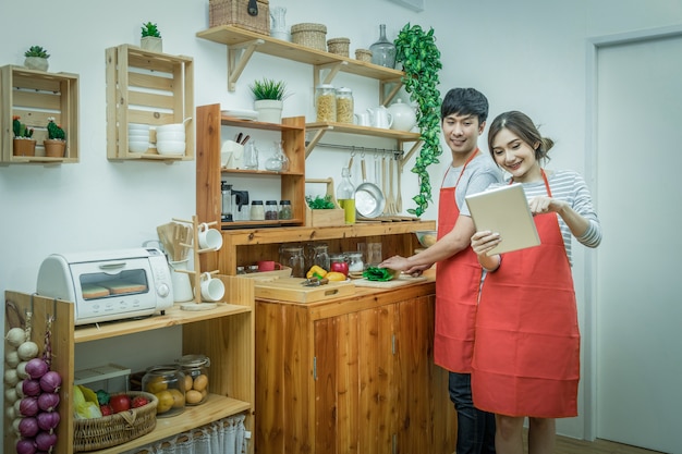 Feliz amante asiático o pareja cocinando y siguiendo el tutorial