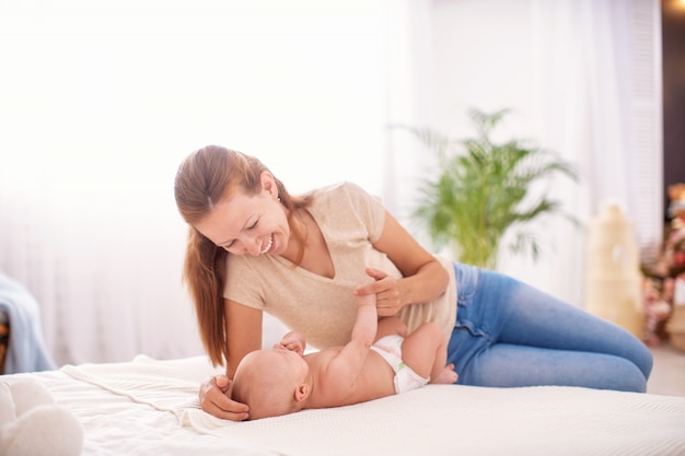 Feliz amorosa familia joven madre juega con su hijo en el dormitorio