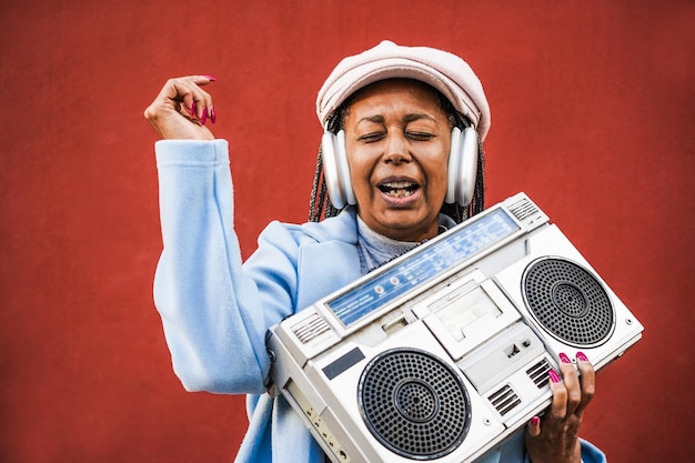 Foto feliz anciana africana escuchando música en estéreo vintage boombox enfoque en la cara