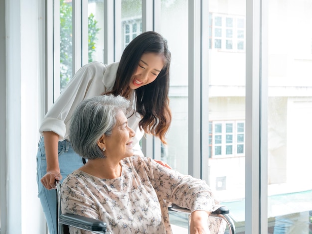 Feliz anciana asiática madre o abuelos en silla de ruedas cuidando de una cuidadora sonriente joven hija o nieta apoyando en casa en el fondo de la naturaleza verde cuidado de la salud de la tercera edad