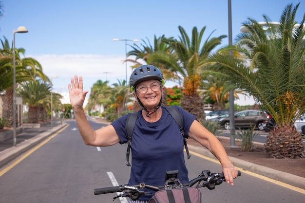 Feliz anciana caucásica con casco y mochila disfrutando de la actividad deportiva con bicicleta eléctrica