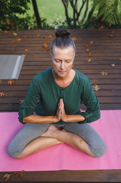 Feliz anciana caucásica practicando yoga, meditando en un jardín soleado. estilo de vida de jubilación saludable, pasar tiempo en casa.