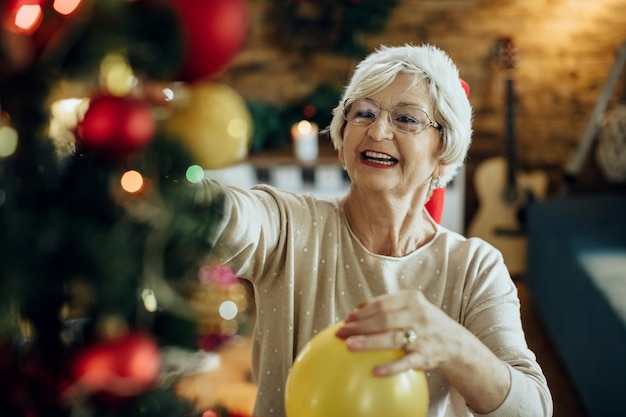 Feliz anciana decorando el árbol de Navidad en casa