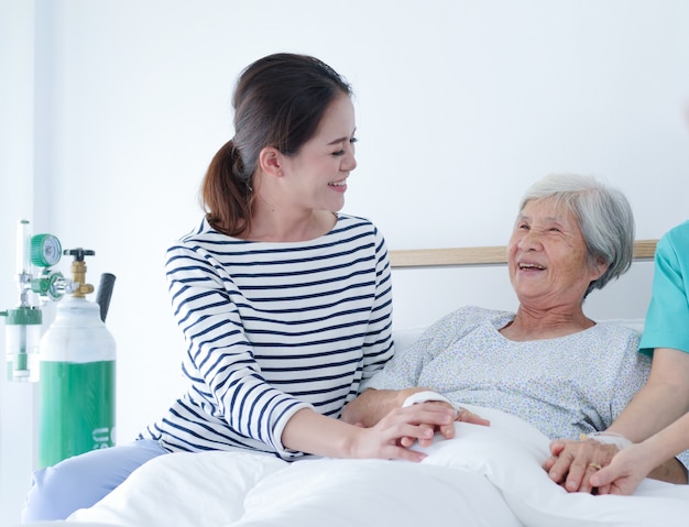 Feliz anciana hablando con la enfermera mayor y su hija en la habitación del hospital.