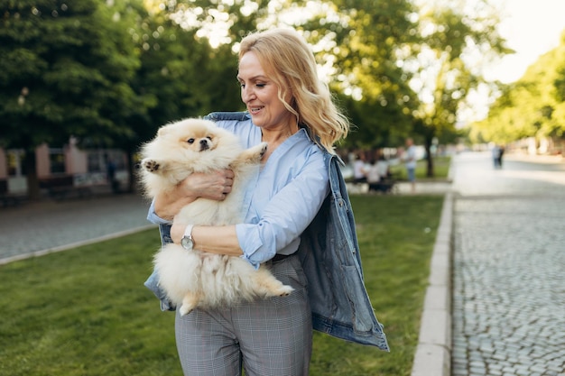 Feliz anciana jubilada sosteniendo un pequeño y lindo cachorro de Pomerania Spitz Hermosa mujer madura con un cachorro en las manos al aire libre Los propietarios se parecen a sus perros Concepto de amor a las mascotas