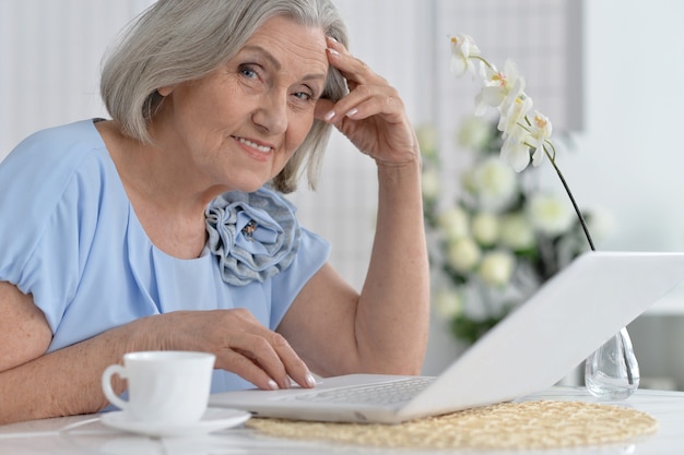 Feliz anciana con laptop en casa