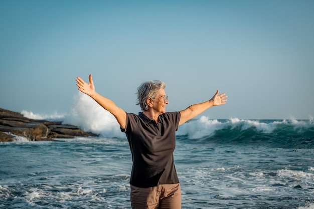 Feliz anciana madura con los brazos extendidos de pie en la playa al atardecer