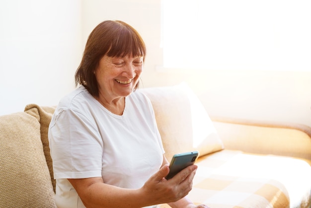 Feliz anciana madura sosteniendo teléfono inteligente con aplicación de teléfono móvil para videollamada riendo mien ...