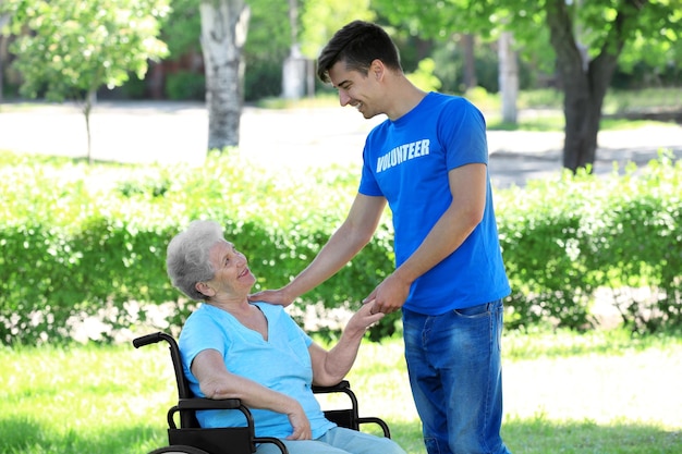 Feliz anciana en silla de ruedas con un joven voluntario al aire libre