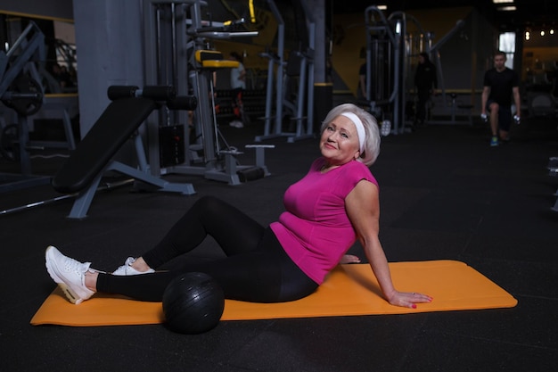 Feliz anciana sonriendo a la cámara descansando después de hacer ejercicio en el gimnasio