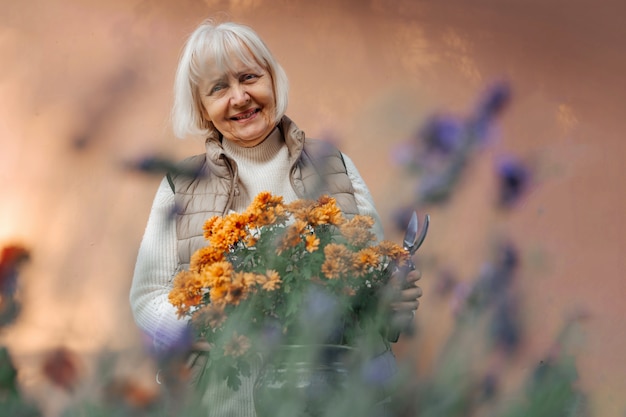 Feliz anciana trabajando con flores en el jardín. Mujer jubilada positiva sonriendo