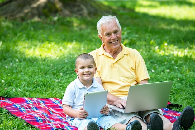 feliz anciano abuelo y niño en el parque usando computadora portátil