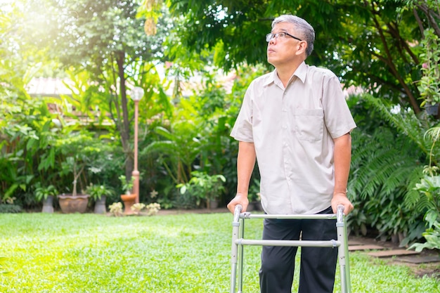 Feliz anciano asiático usa un andador y camina en el patio trasero