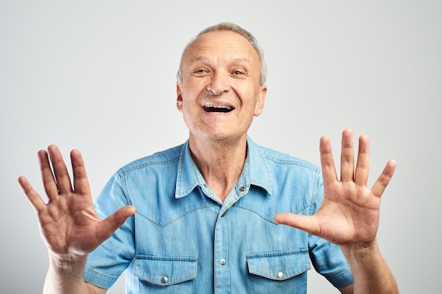 Foto feliz anciano canoso muestra diez dedos y se ríe alegremente aislado en un fondo blanco, pide que se detenga