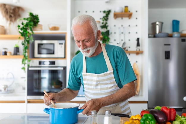 Feliz anciano divirtiéndose cocinando en casa Anciano preparando almuerzo saludable en cocina moderna Tiempo de estilo de vida jubilado y concepto de nutrición alimentaria