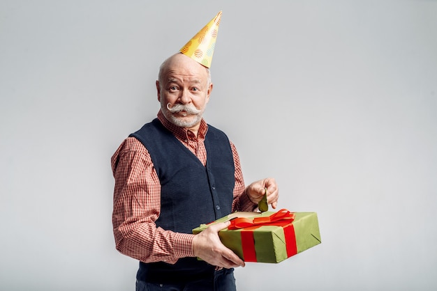 Feliz anciano en gorra de fiesta tiene caja de regalo