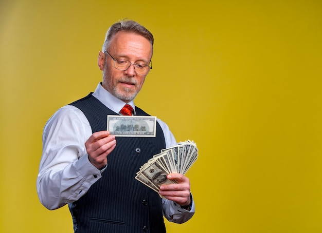 Feliz anciano hombre de negocios con abanico de billetes de dólar aislado sobre fondo amarillo Hombre mayor ganó la lotería Día de la suerte Emociones humanas y expresiones faciales