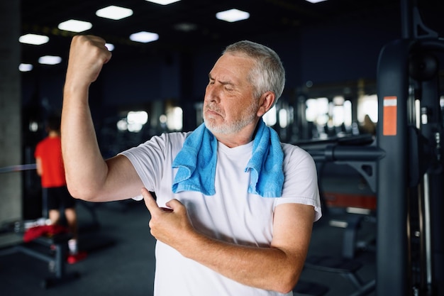 Feliz anciano muestra sus músculos en el gimnasio