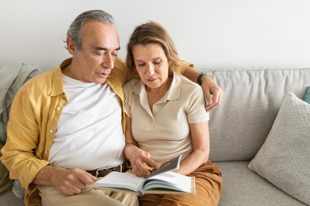 Feliz anciano y mujer abrazándose y relajándose juntos en el sofá disfrutando leyendo literatura favorita