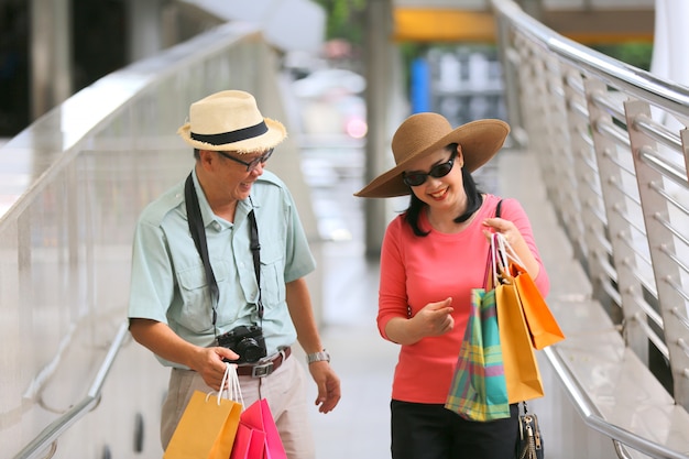 Feliz anciano y una mujer caminando en la calle en un día de verano. Relajado pareja senior con sombreros ir de compras.