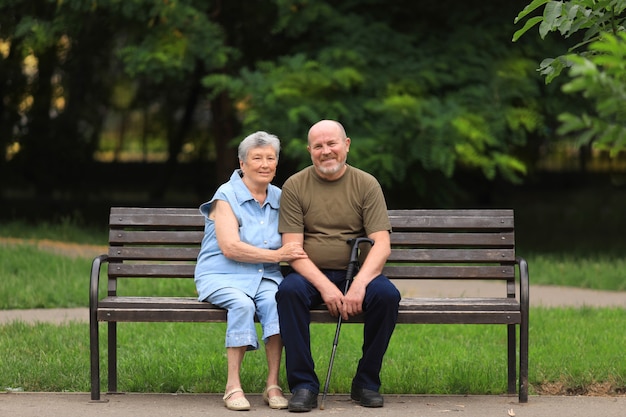 Feliz anciano y mujer discapacitada se sientan en un banco al aire libre en el parque de verano