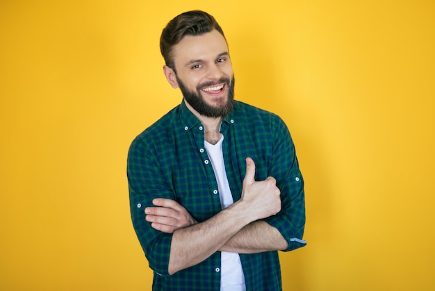 Feliz, animado, bonito, barbudo, homem moderno com a camisa quadriculada está posando e mostrando o polegar