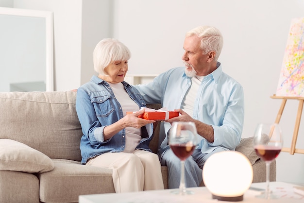 Feliz aniversário. encantador homem idoso parabenizando sua amada esposa com aniversário de casamento e dando a ela uma caixa lindamente embrulhada com um presente