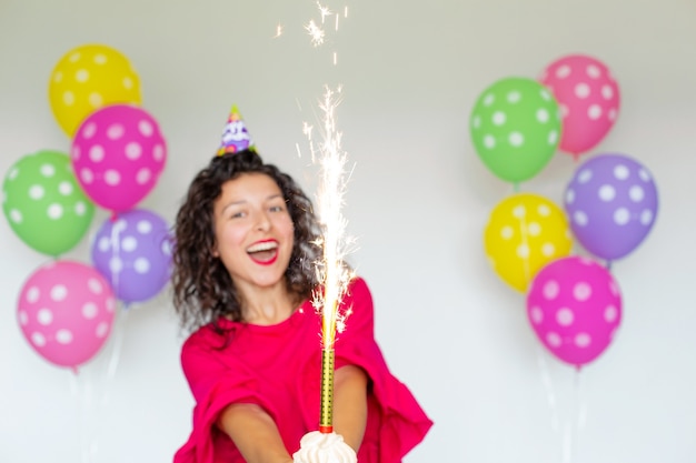 Feliz Aniversário. Garota morena sexy posando com balões, fogos de artifício, balões coloridos e bolo de férias em um fundo branco.