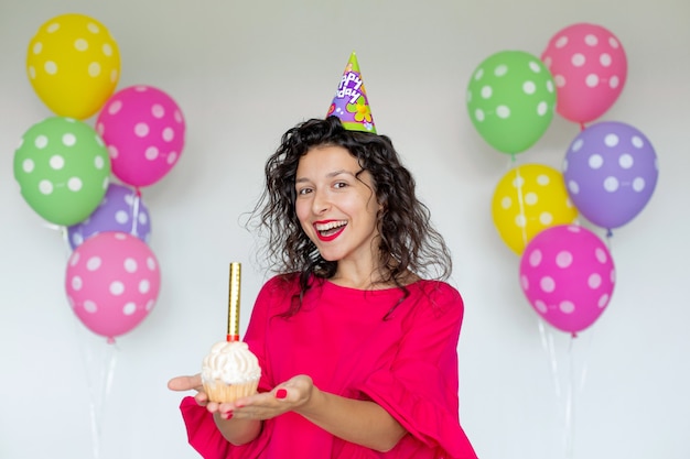 Feliz aniversário. Garota morena sexy posando com balões, fogos de artifício, balões coloridos e bolo de férias em um fundo branco