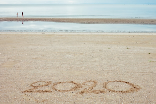 Feliz ano novo 2020, letras na praia com ondas e mar azul claro.