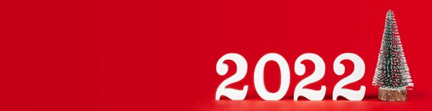 Feliz ano novo 2022. banner retangular longo vermelho brilhante com números de madeira brancos 2022 suporte com árvore de natal de brinquedo. feliz natal. copie o espaço. lugar para texto