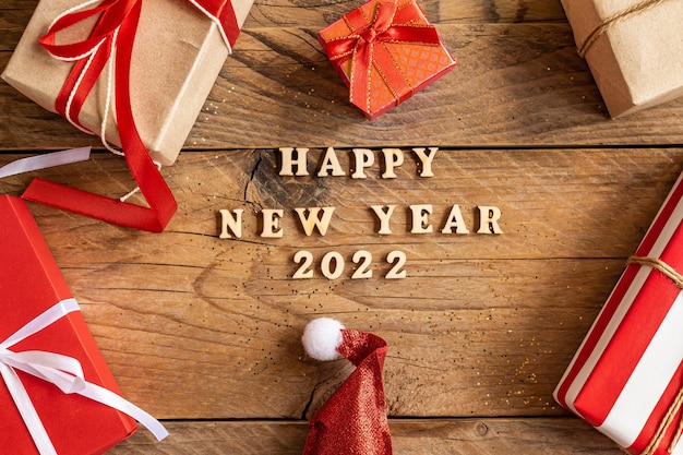 Feliz ano novo 2022. citação feita de letras de madeira e números 2022 em fundo de madeira com caixas de presente multicoloridas. conceito criativo para cartão de ano novo