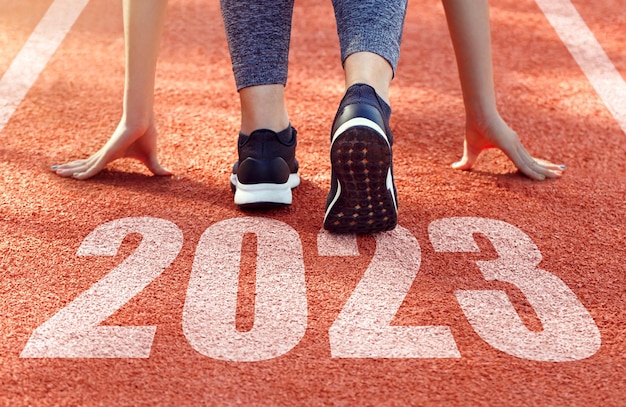 Foto feliz ano novo 2023 vista traseira de uma mulher se preparando para começar em uma pista de atletismo gravada