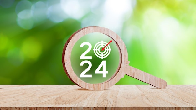 Feliz ano novo 2024 com banner de conceito de negócio número do ano 2024 com ícone Target dentro da lupa de madeira no fundo da mesa de madeira Planejamento para conceitos de objetivo e sucesso