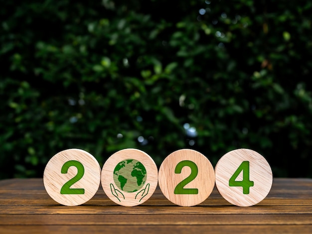 Foto feliz ano novo 2024 com o cuidado mundial conceitos de sustentabilidade ambiental verde 2024 números e símbolo de cuidado da terra em blocos de madeira ecológicos circulares em fundo de folhas verdes de mesa de madeira