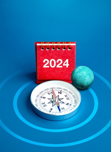 Foto feliz ano novo 2024 fundo de banner vertical globo 3d 2024 números ano no suporte de capa de calendário de mesa vermelho e bússola no alvo de dardos alvo e fundo azul conceitos de metas de negócios em todo o mundo