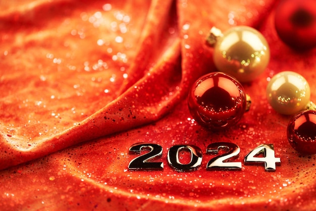 Foto feliz ano novo 2024 números brilhantes em um fundo de tecido vermelho com decorações de natal