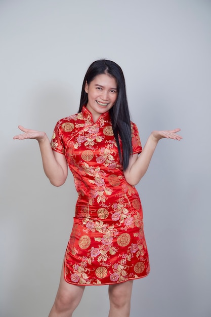 Feliz Ano Novo Chinês. Linda mulher asiática com vestido tradicional cheongsam qipao com gesto de parabéns, isolado em uma superfície cinza claro com espaço de cópia