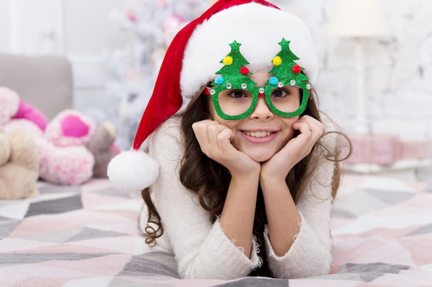 Feliz Ano Novo. Lista de Desejos. Atmosfera de férias. Espirito natalino. Feriado de ano novo. Criança pequena usar chapéu de Papai Noel comemorar o ano novo em casa decorada com fundo interior. Menina criança no quarto com brinquedos.