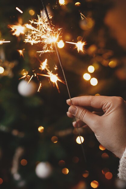 Feliz ano novo mão segurando estrelinha acesa nas luzes da árvore de natal na sala festiva atmosférica